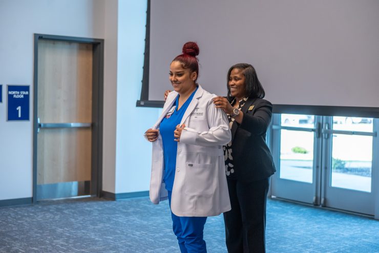 Dr. Sabrina Pope, Methodist University's Clinical Coordinator & Assistant Professor of Nursing, provides a white coat to a Cape Fear Valley Health nurse to mark the beginning of the new nursing partnership between the two institutions.